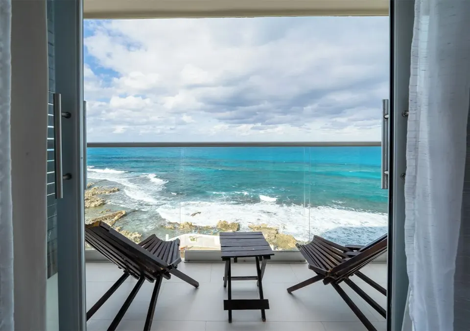 Balcony ocean view from a Deluxe Room at Mia Reef Isla Mujeres with lounge chairs and waves below.