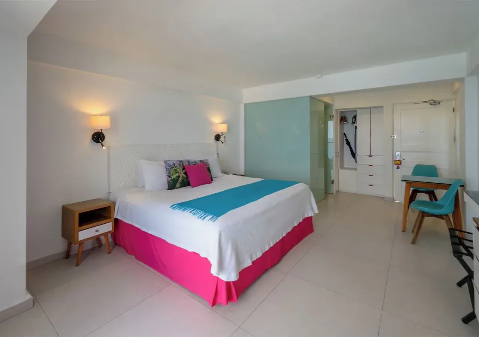 Deluxe Room Ocean View at Mia Reef Isla Mujeres with a king bed, bedside lighting, desk, and entry area.