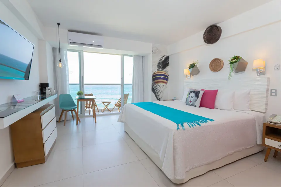 Deluxe Room Ocean View at Mia Reef Isla Mujeres with a king bed, wall-mounted TV, and balcony beyond.