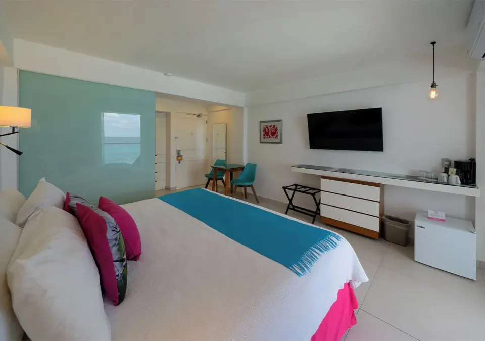 Deluxe Room Ocean View at Mia Reef Isla Mujeres with a king bed, TV wall, minibar area, and small table.