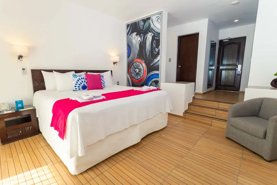 Deluxe Villa Ocean Front Suite king bed with armchair and entry steps at Mia Reef Isla Mujeres.