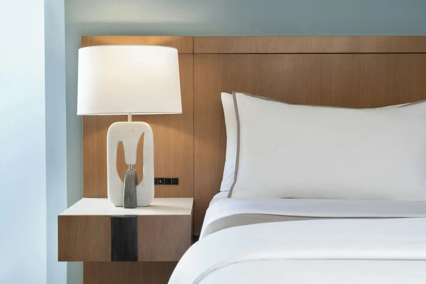 Guest room bed and bedside lamp at Moana Surfrider, A Westin Resort & Spa.