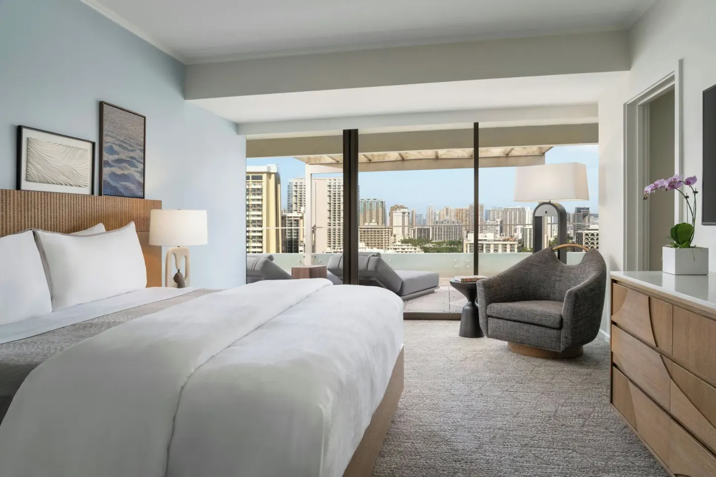 King bed with city-view balcony and sitting chair at Moana Surfrider, A Westin Resort & Spa.