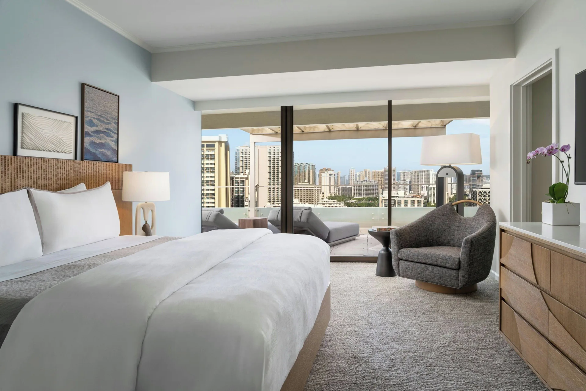 King bed with city-view balcony and sitting chair at Moana Surfrider, A Westin Resort & Spa.