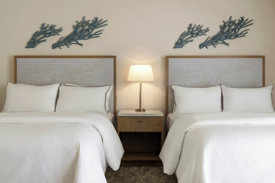 Two beds with coral wall decor and a shared nightstand at Moana Surfrider, A Westin Resort & Spa.