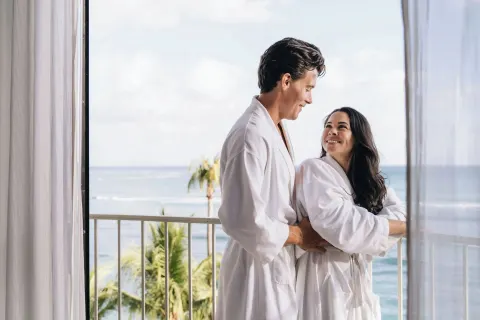 Couple in robes on an ocean-view balcony at Moana Surfrider, A Westin Resort & Spa.
