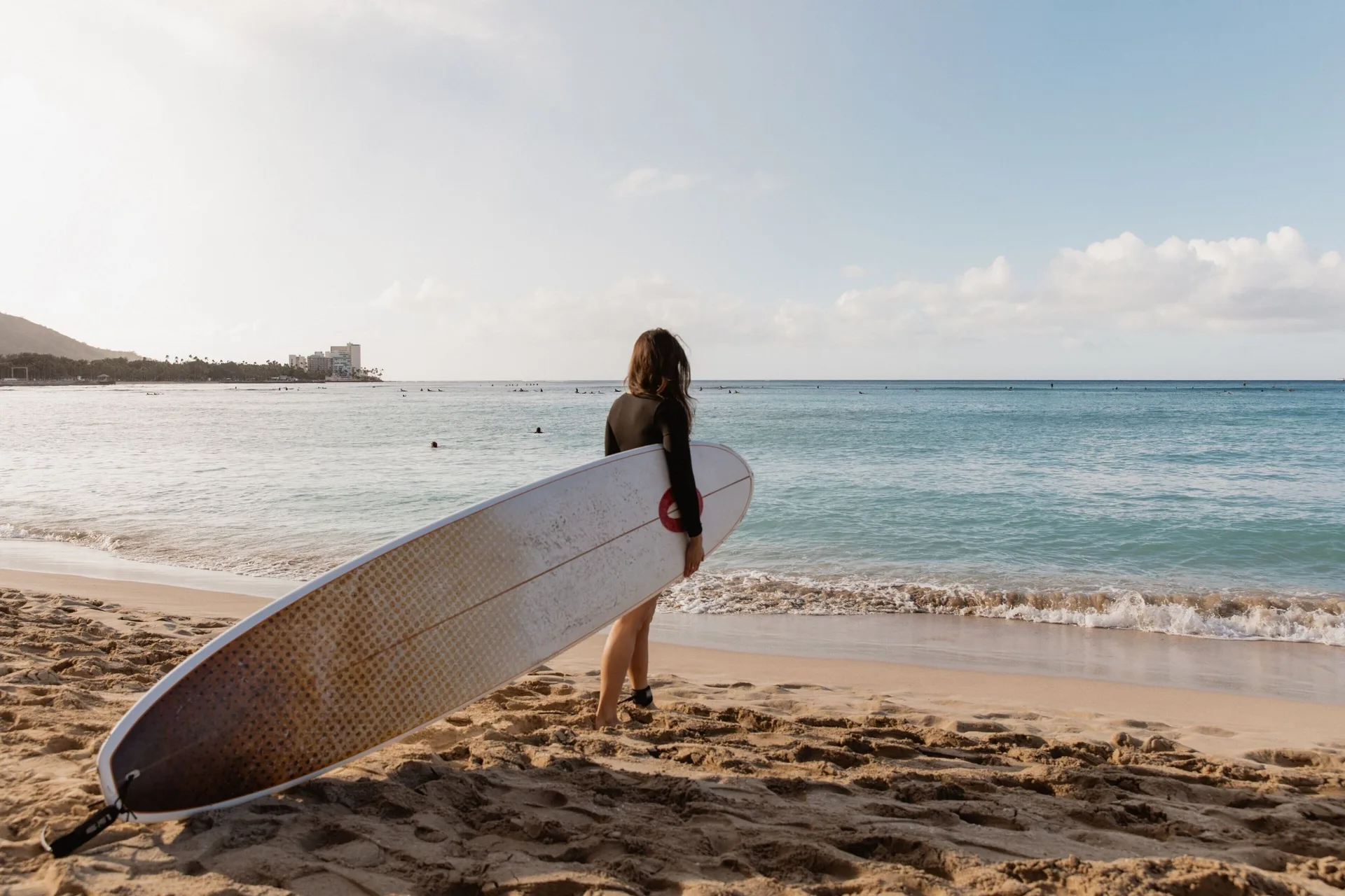 Surfer holding a longboard on the beach near Moana Surfrider, A Westin Resort & Spa.