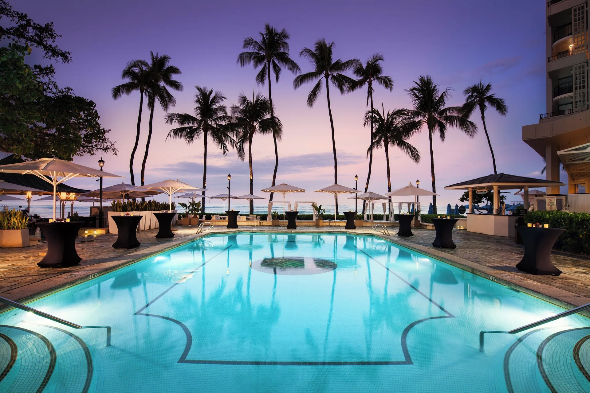 Twilight pool with palm trees and ocean beyond at Moana Surfrider, A Westin Resort & Spa.