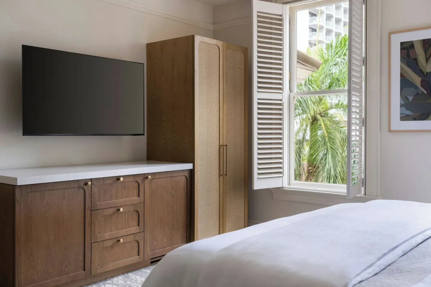 Banyan Deluxe Room bed, TV, wardrobe, and shuttered window at Moana Surfrider, A Westin Resort & Spa.