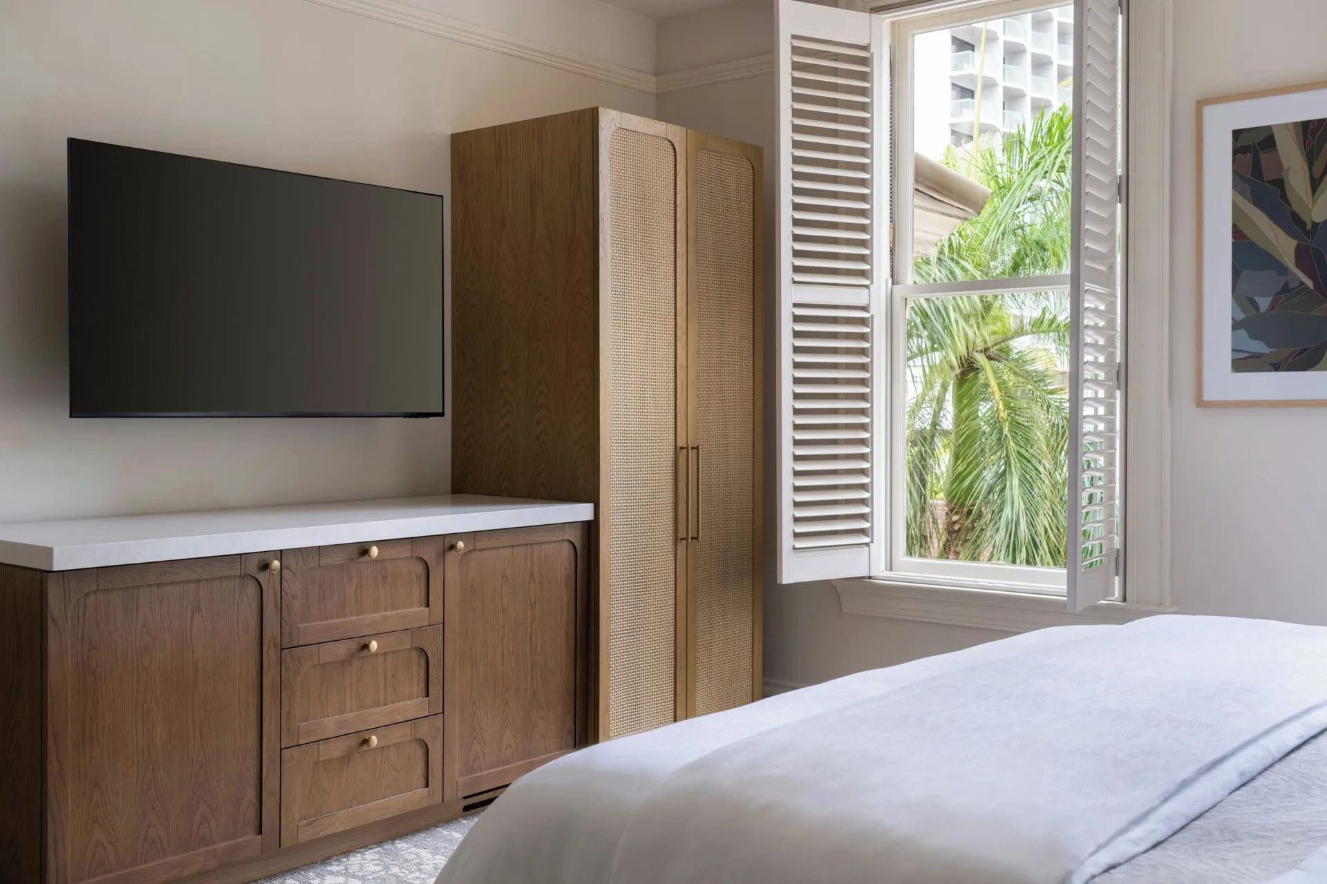 Banyan Deluxe Room bed, TV, wardrobe, and shuttered window at Moana Surfrider, A Westin Resort & Spa.