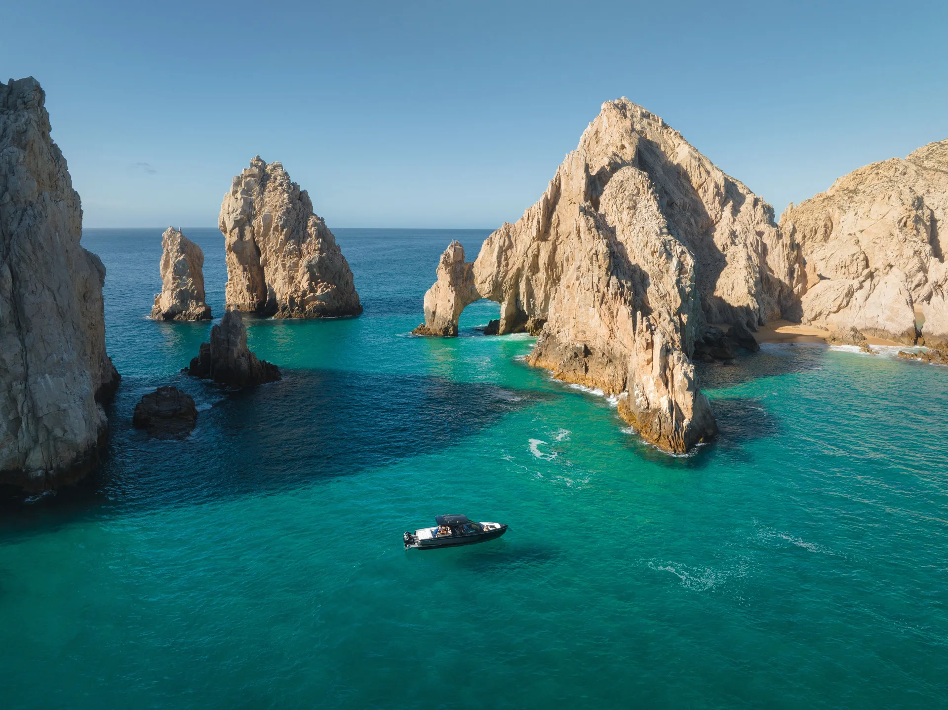 Turquoise water, rock arches, and a boat near Cabo’s coastal formations by Montage Los Cabos.