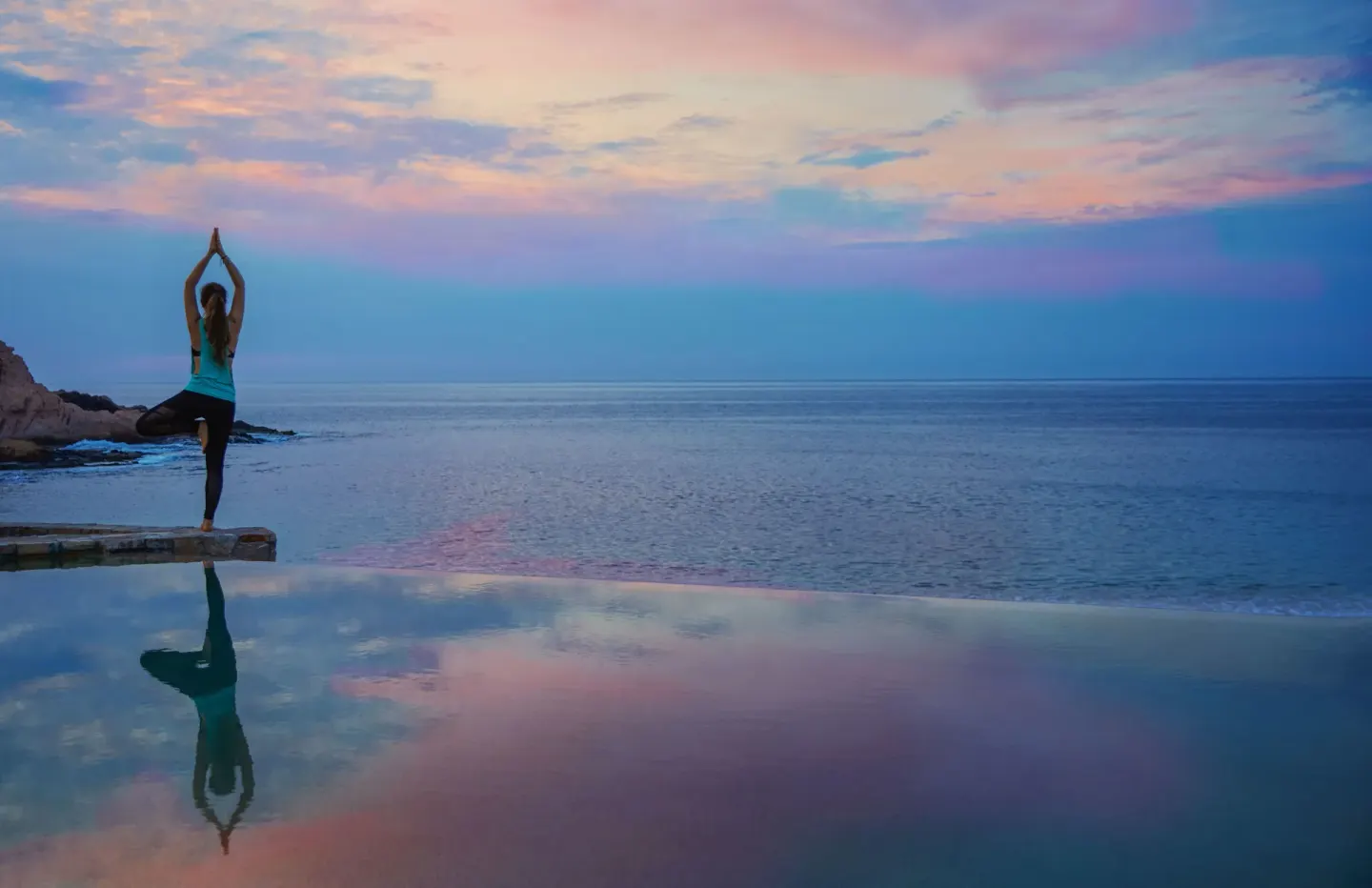 Person doing yoga beside an infinity pool at sunset at Montage Los Cabos.
