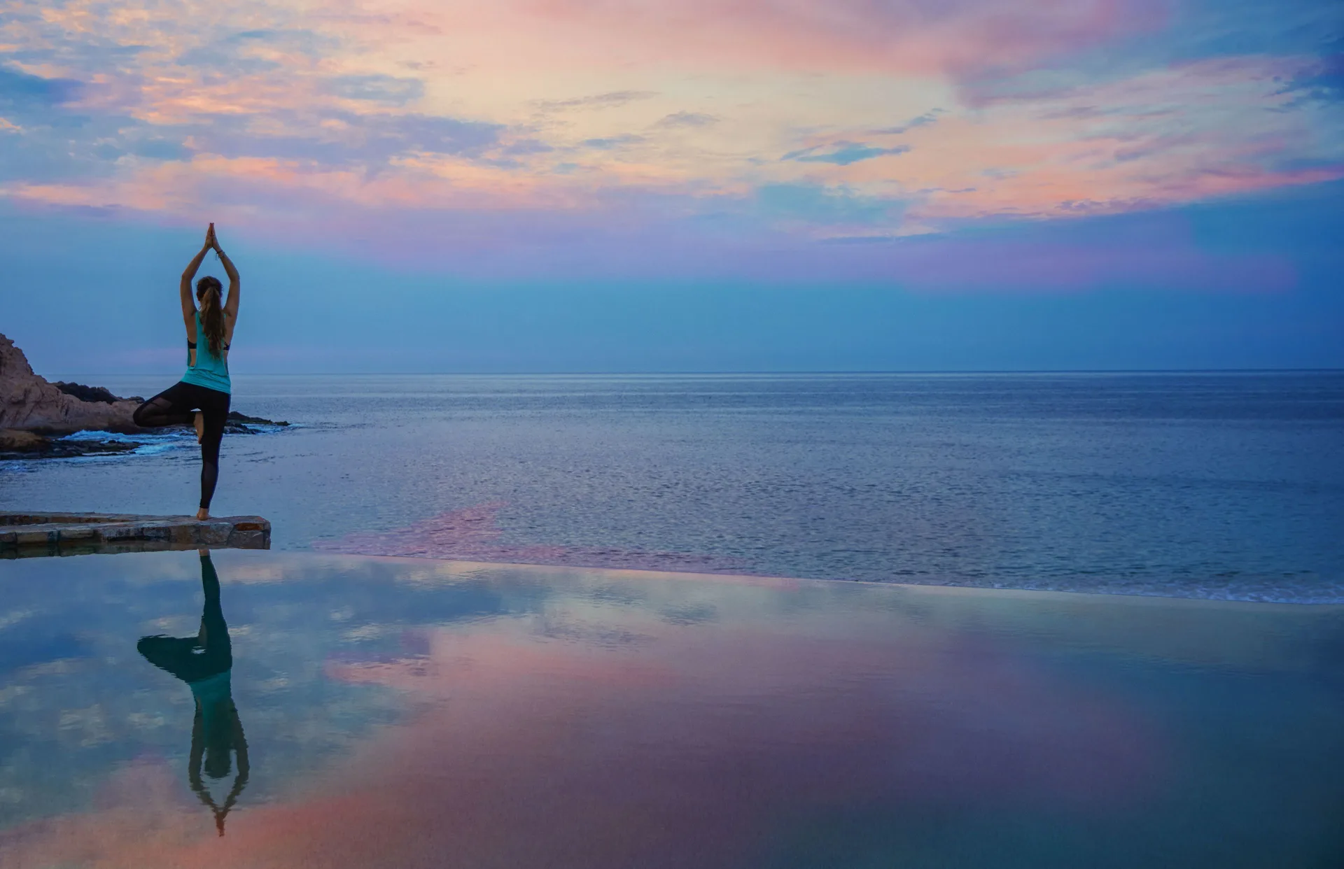 Person doing yoga beside an infinity pool at sunset at Montage Los Cabos.