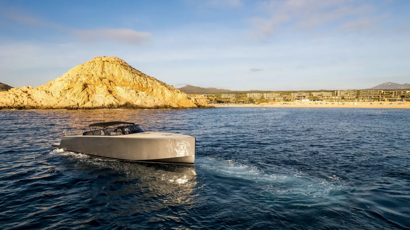 Motor yacht cruising offshore with Montage Los Cabos and rocky coastline in the distance.