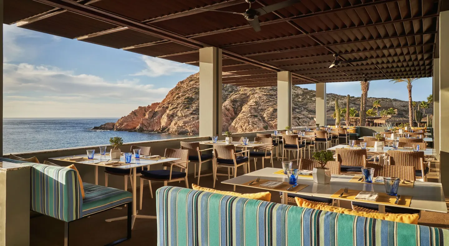 An open-air restaurant terrace overlooks the ocean and rocky cove at Montage Los Cabos.