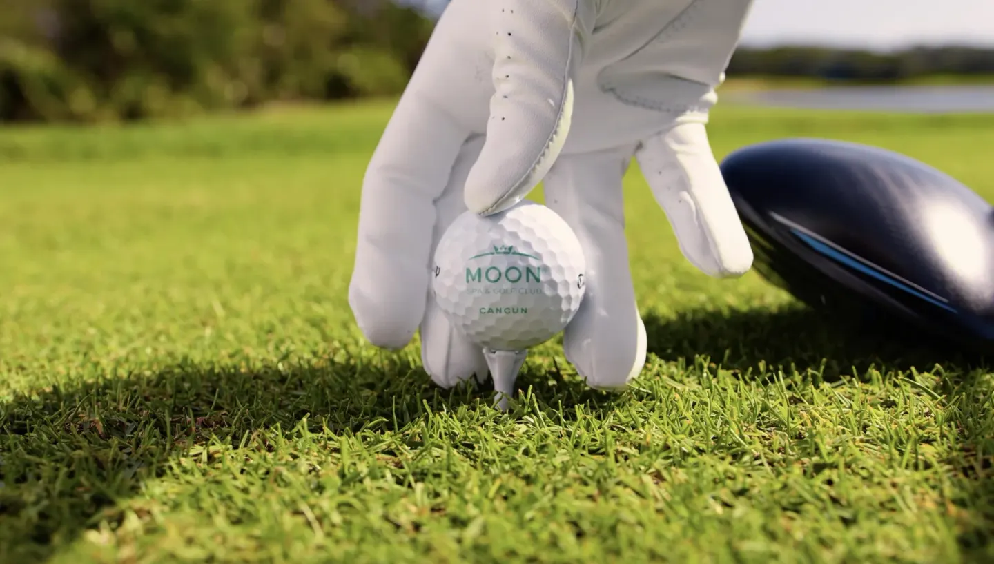 A gloved hand tees up a golf ball on the grass at Moon Palace Cancun.