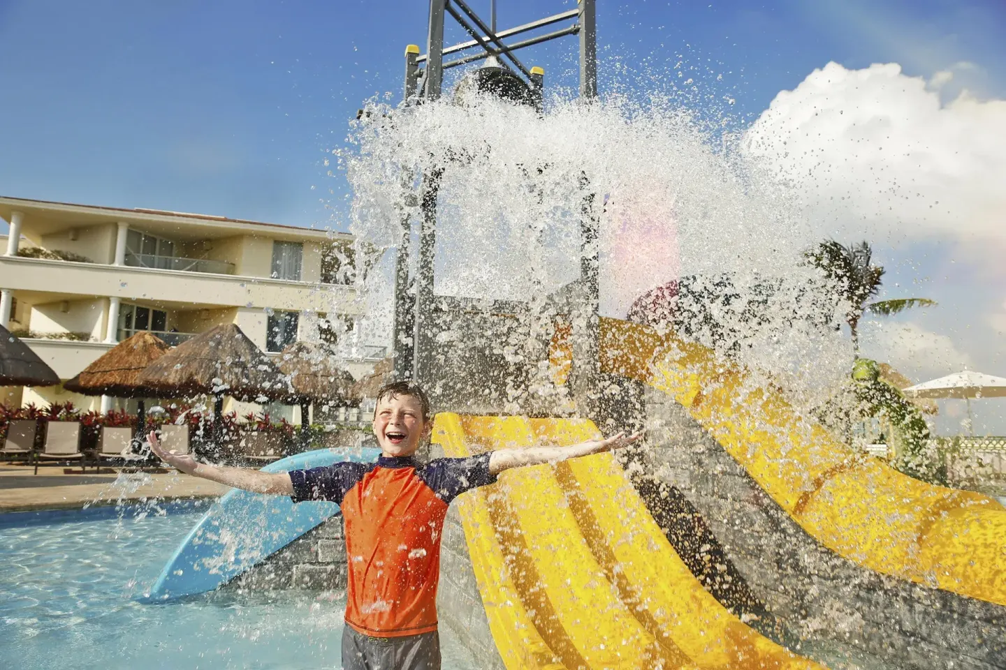 Child playing under a splash bucket beside yellow slides at Moon Palace Cancun.