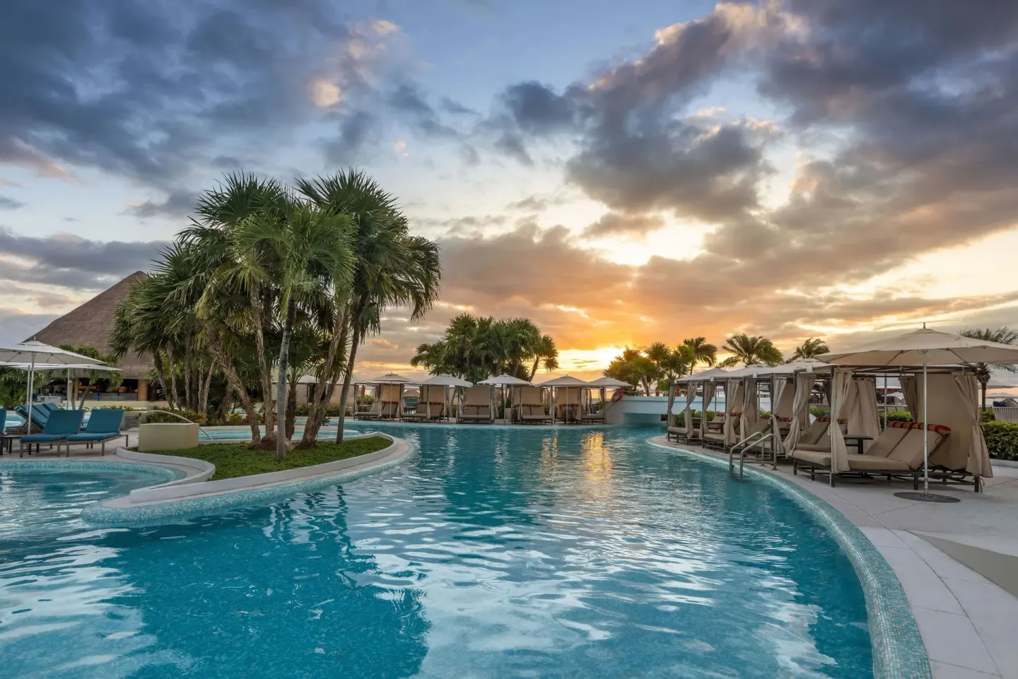 Curving resort pool with cabanas and palms at sunset at Moon Palace Cancun.