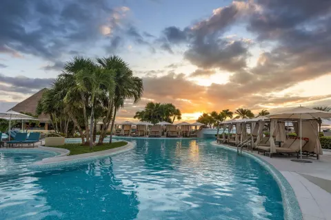 Curving resort pool with cabanas and palms at sunset at Moon Palace Cancun.