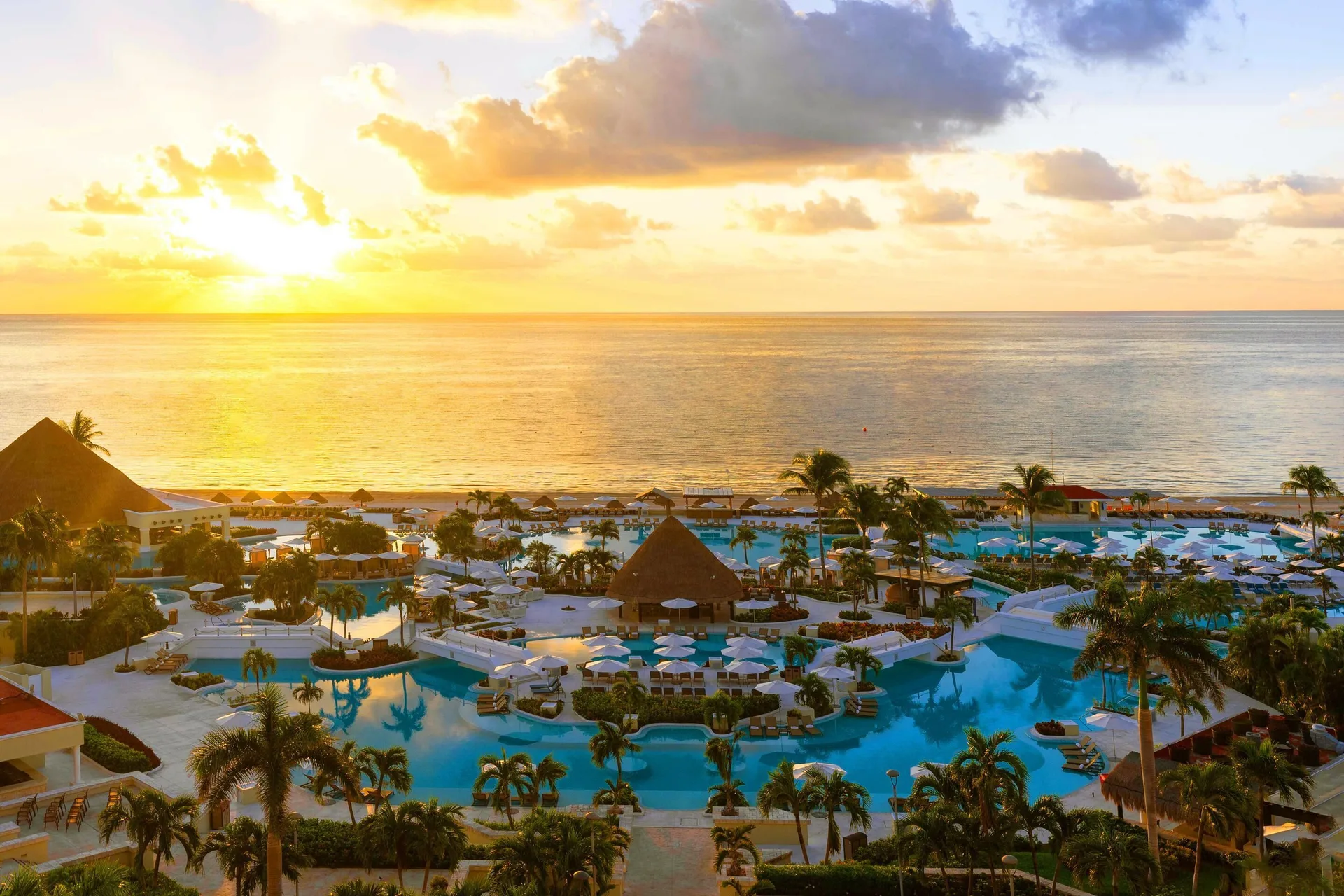 Sunrise over the ocean, pools, palms, and palapas at Moon Palace Cancun.