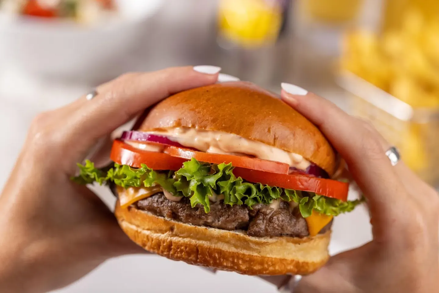 Hands hold a cheeseburger with lettuce and tomato at Moon Palace Cancun.