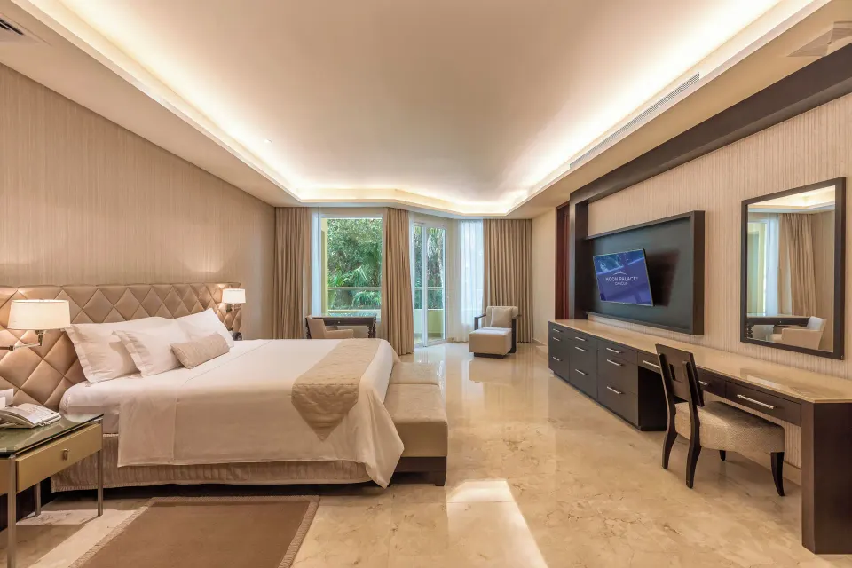 Spacious king bedroom with desk, TV, and balcony windows at Moon Palace Cancun.
