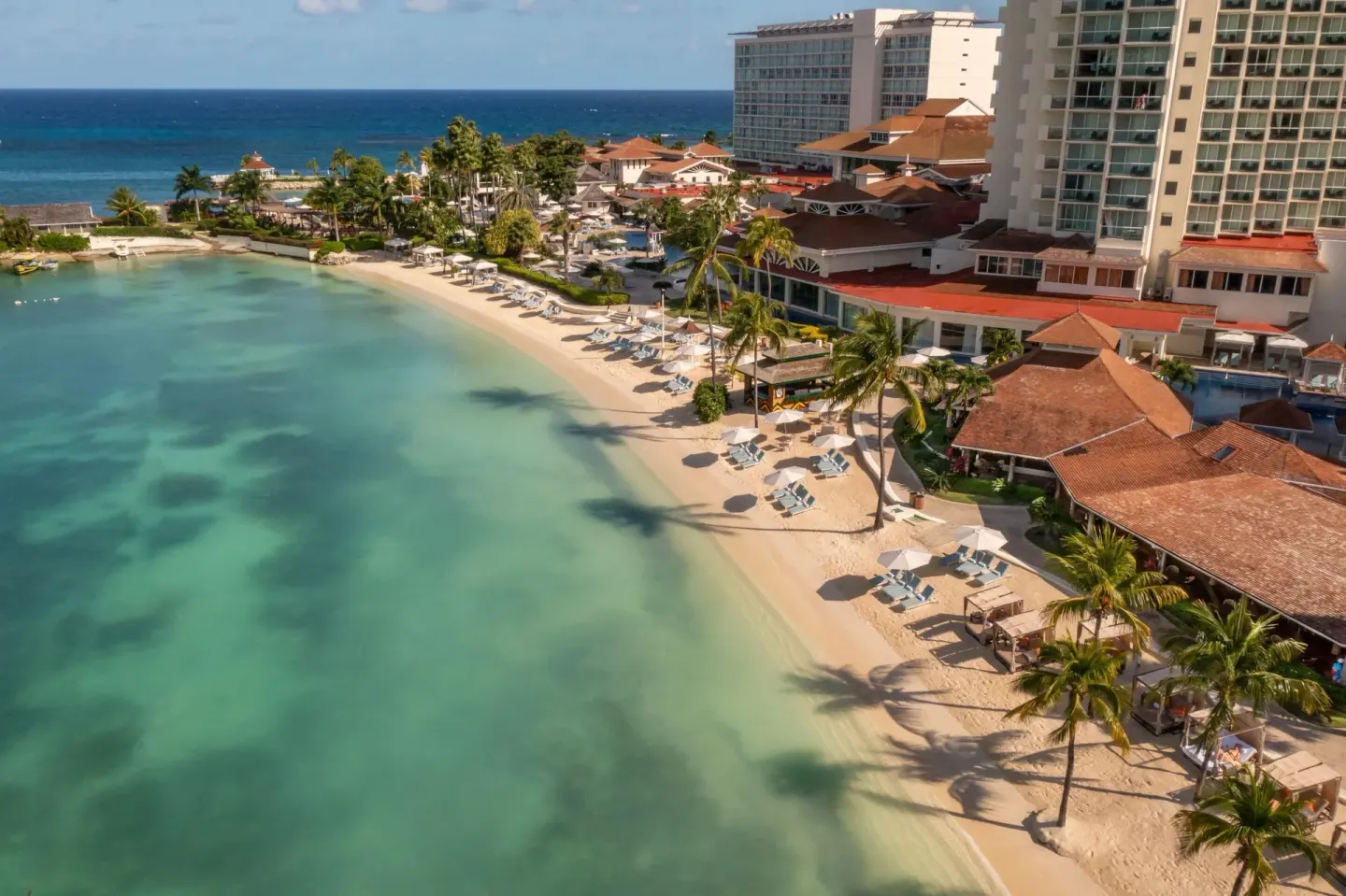 An aerial view of the beach, clear water, palms, and resort buildings at Moon Palace Jamaica.