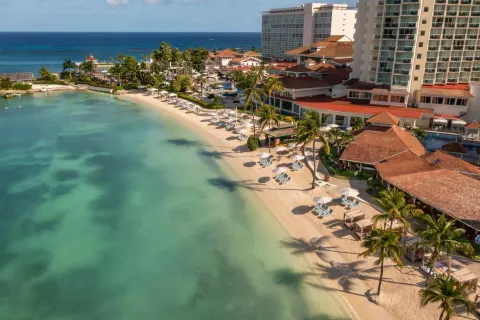 An aerial view of the beach, clear water, palms, and resort buildings at Moon Palace Jamaica.