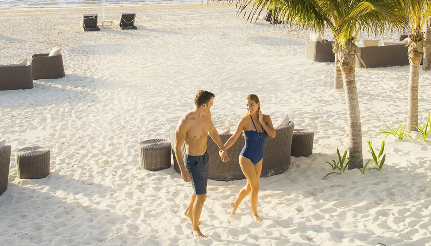 A couple walks past lounge seating on the sandy beach at Moon Palace Jamaica.