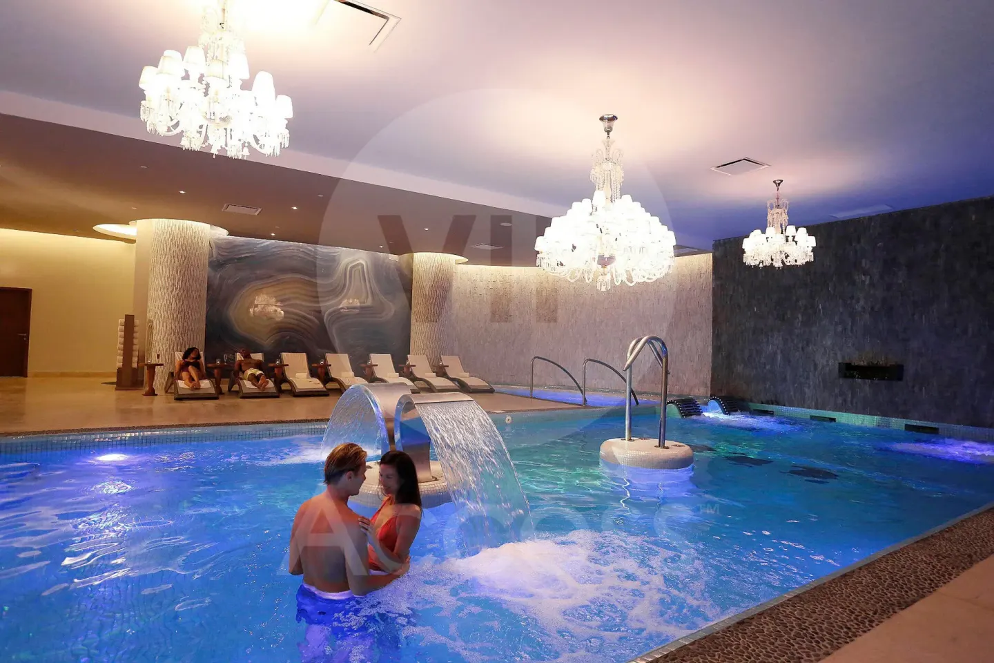 Indoor spa pool with chandeliers, loungers, and guests in the water at Moon Palace Jamaica.