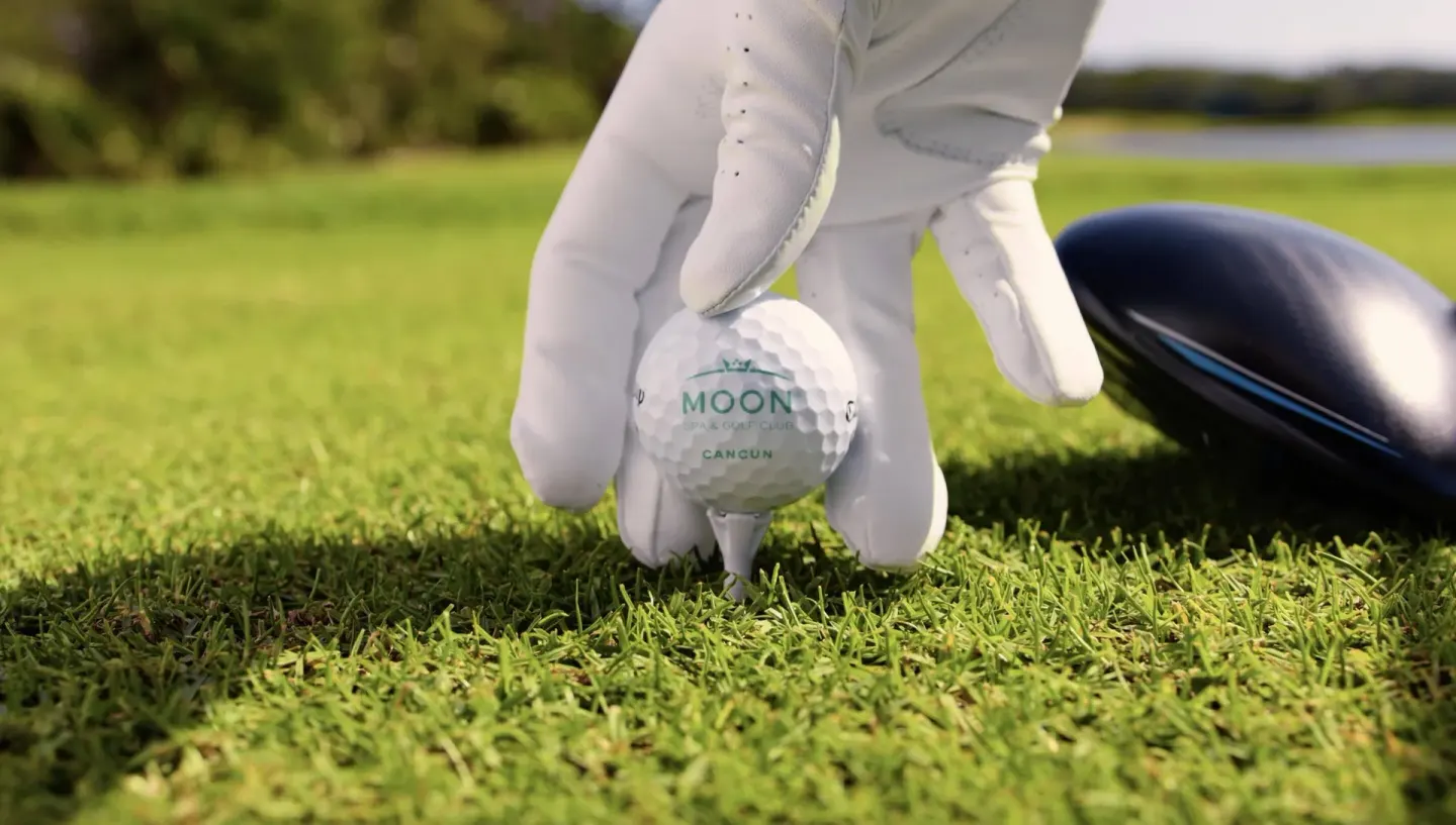 Gloved hand placing a golf ball on a tee at Moon Palace Nizuc.