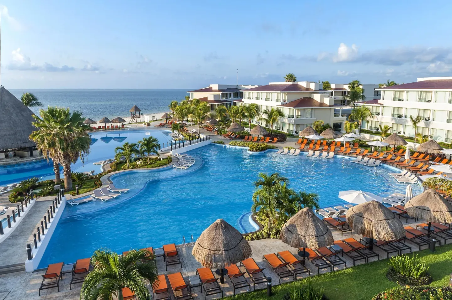 Large pool complex with palapas, loungers, palms, and ocean beyond at Moon Palace Nizuc.