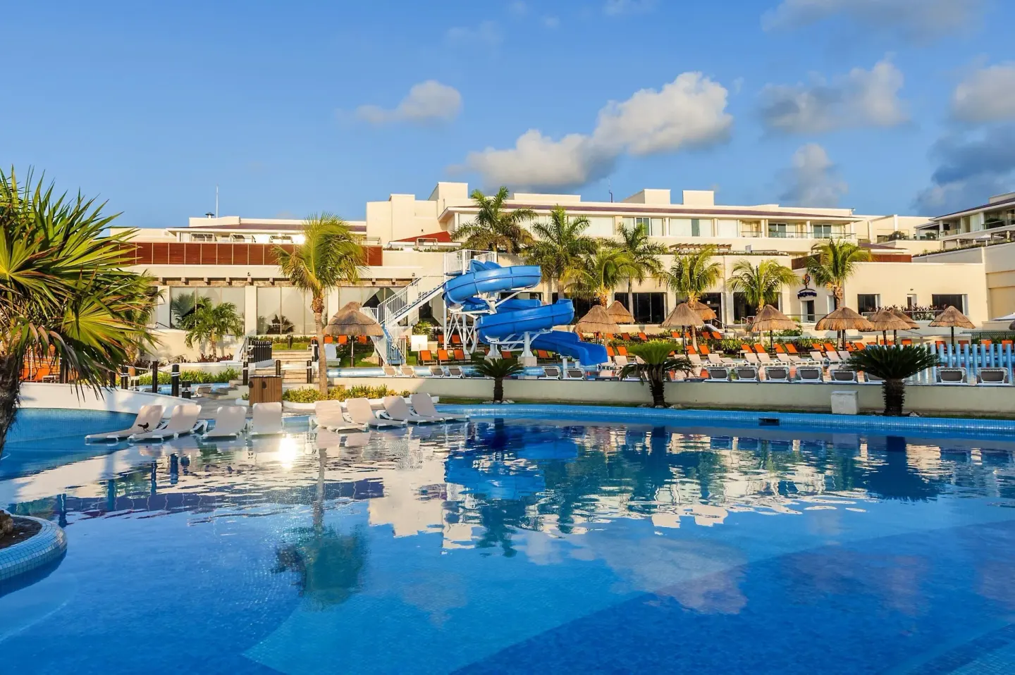 Pool with blue waterslides, loungers, palms, and resort buildings at Moon Palace Nizuc.
