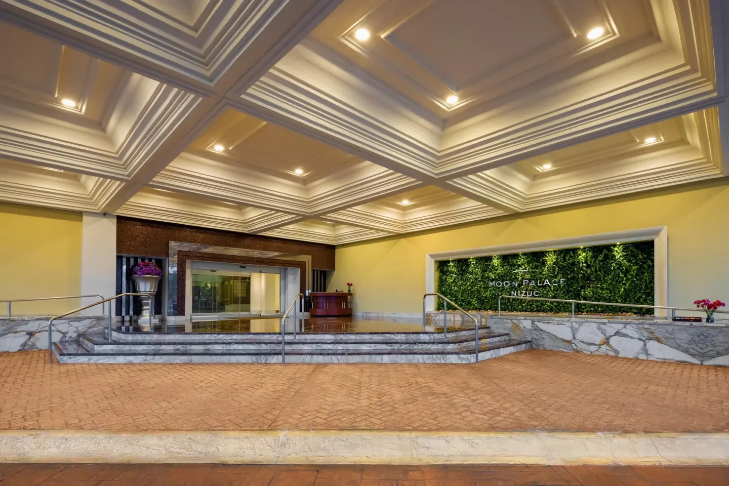 Covered entrance with marble steps and green wall sign at Moon Palace Nizuc.
