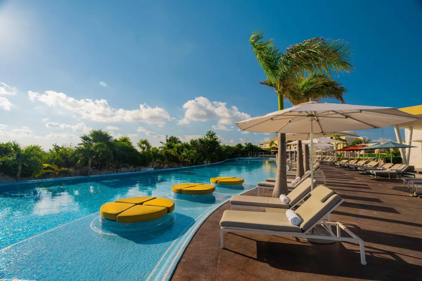 Curving pool with yellow in-water seats and shaded loungers at Moon Palace The Grand Cancun.
