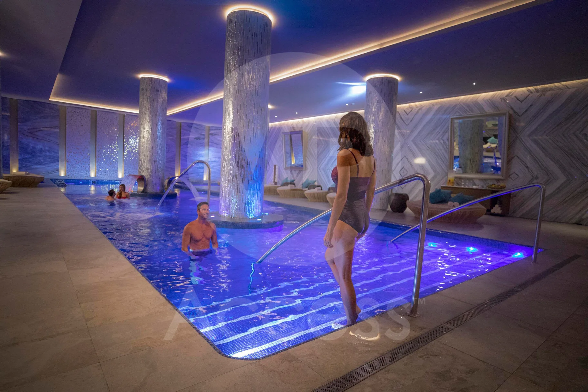 Guests using an indoor blue-lit spa pool with column features at Moon Palace The Grand Cancun.