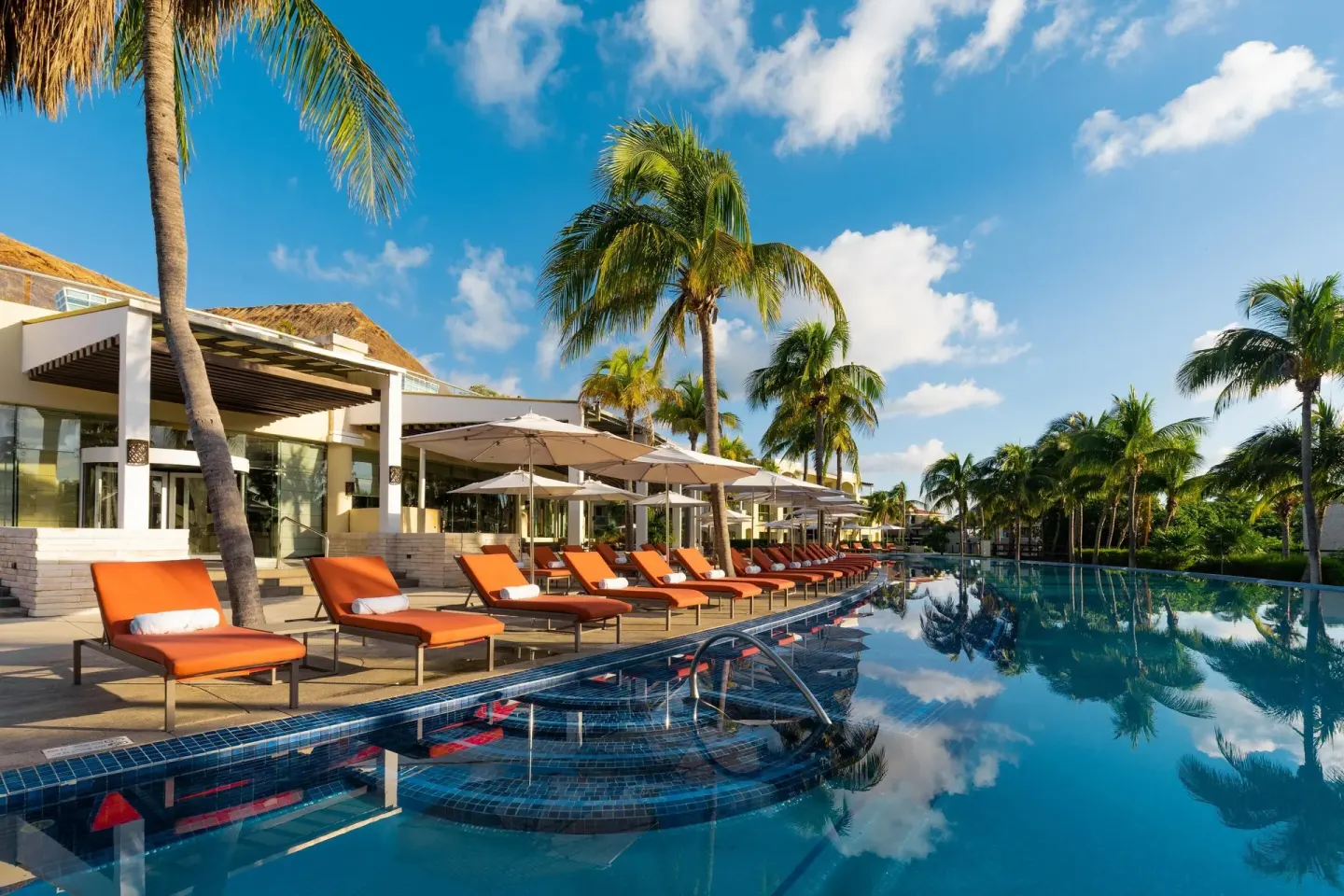 Long resort pool with orange loungers and palm trees at Moon Palace The Grand Cancun.