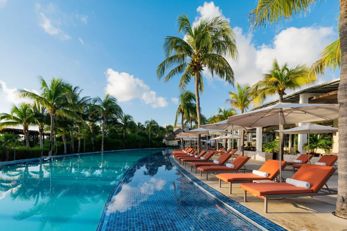 Palm-lined pool with orange loungers and white umbrellas at Moon Palace The Grand Cancun.