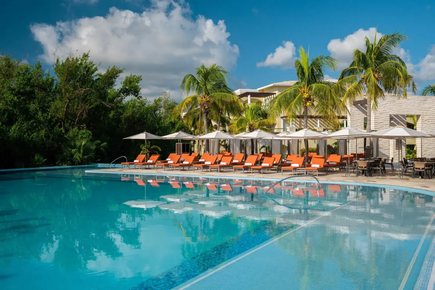 Pool deck with orange loungers, umbrellas, and palms at Moon Palace The Grand Cancun.
