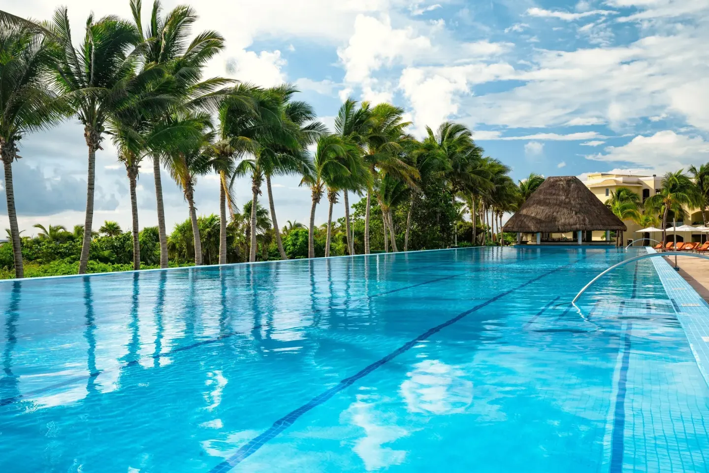 Wide infinity-style pool with palms and a thatched structure at Moon Palace The Grand Cancun.