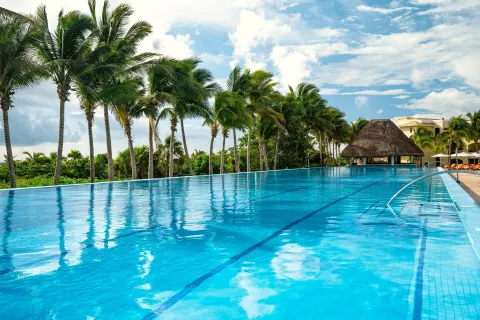 Wide infinity-style pool with palms and a thatched structure at Moon Palace The Grand Cancun.