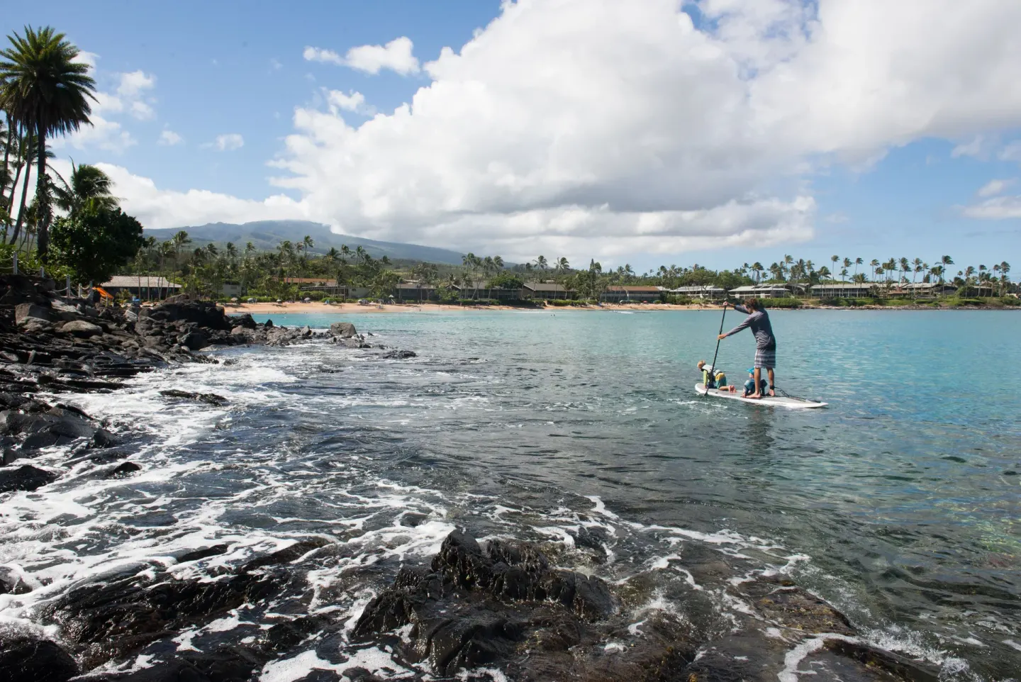 Rocky shoreline and paddleboarder near the beach at Napili Kai Beach Resort.