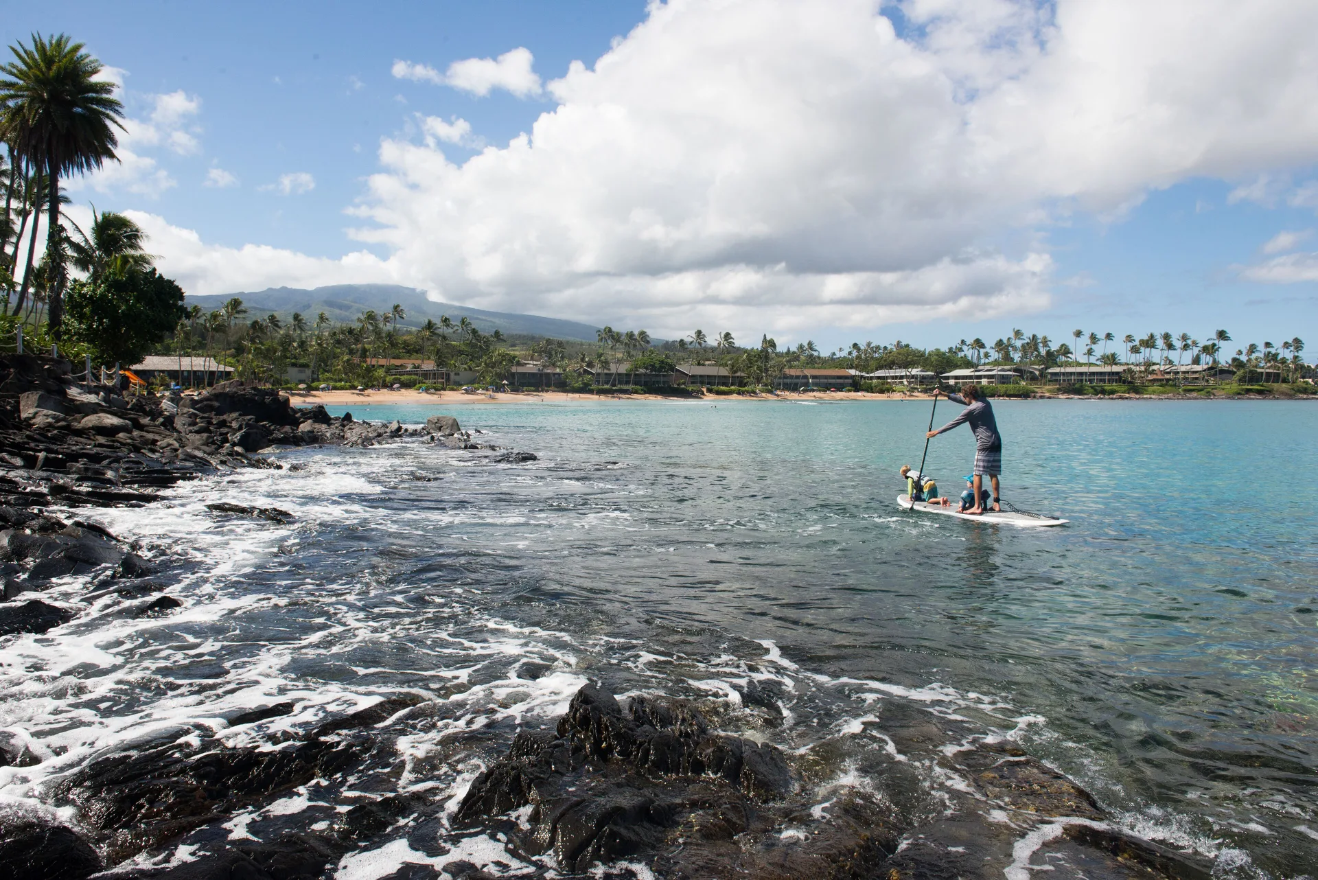Rocky shoreline and paddleboarder near the beach at Napili Kai Beach Resort.