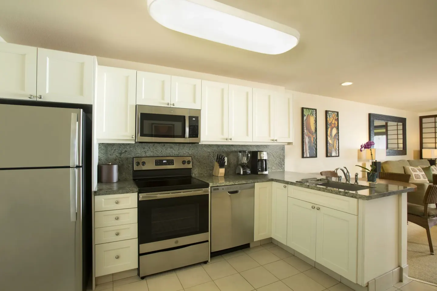 Bright kitchen at Napili Kai Beach Resort with white cabinets, stainless appliances, and an island sink.