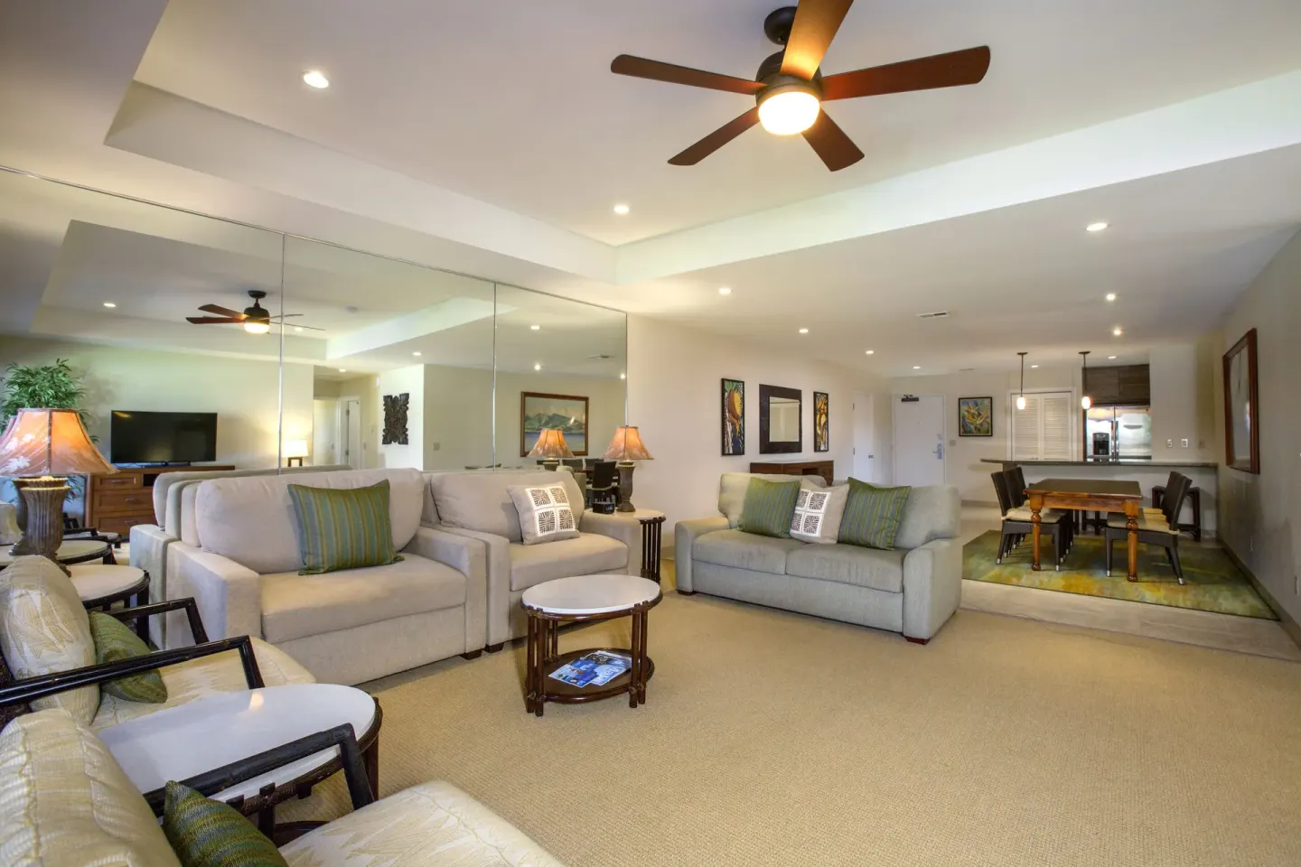 Living and dining area at Napili Kai Beach Resort with sofas, armchairs, mirrors, and kitchen beyond.