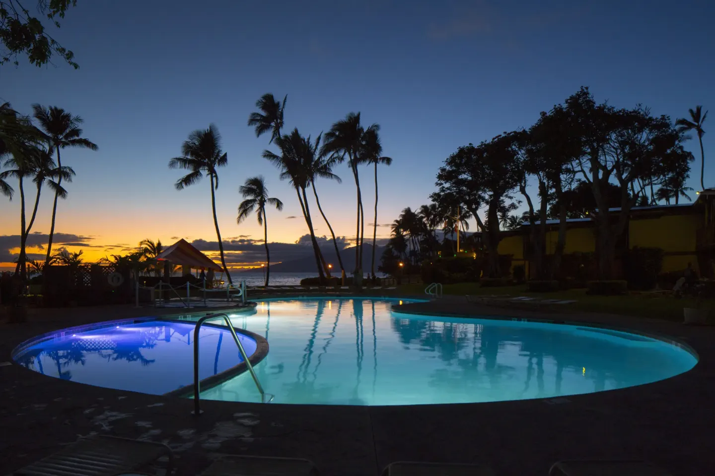 Pool glowing at sunset with palm silhouettes at Napili Kai Beach Resort.