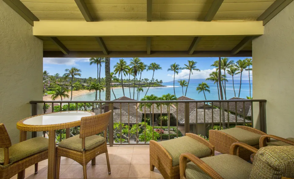 Deluxe Room balcony with wicker seating and palm-framed bay view at Napili Kai Beach Resort.
