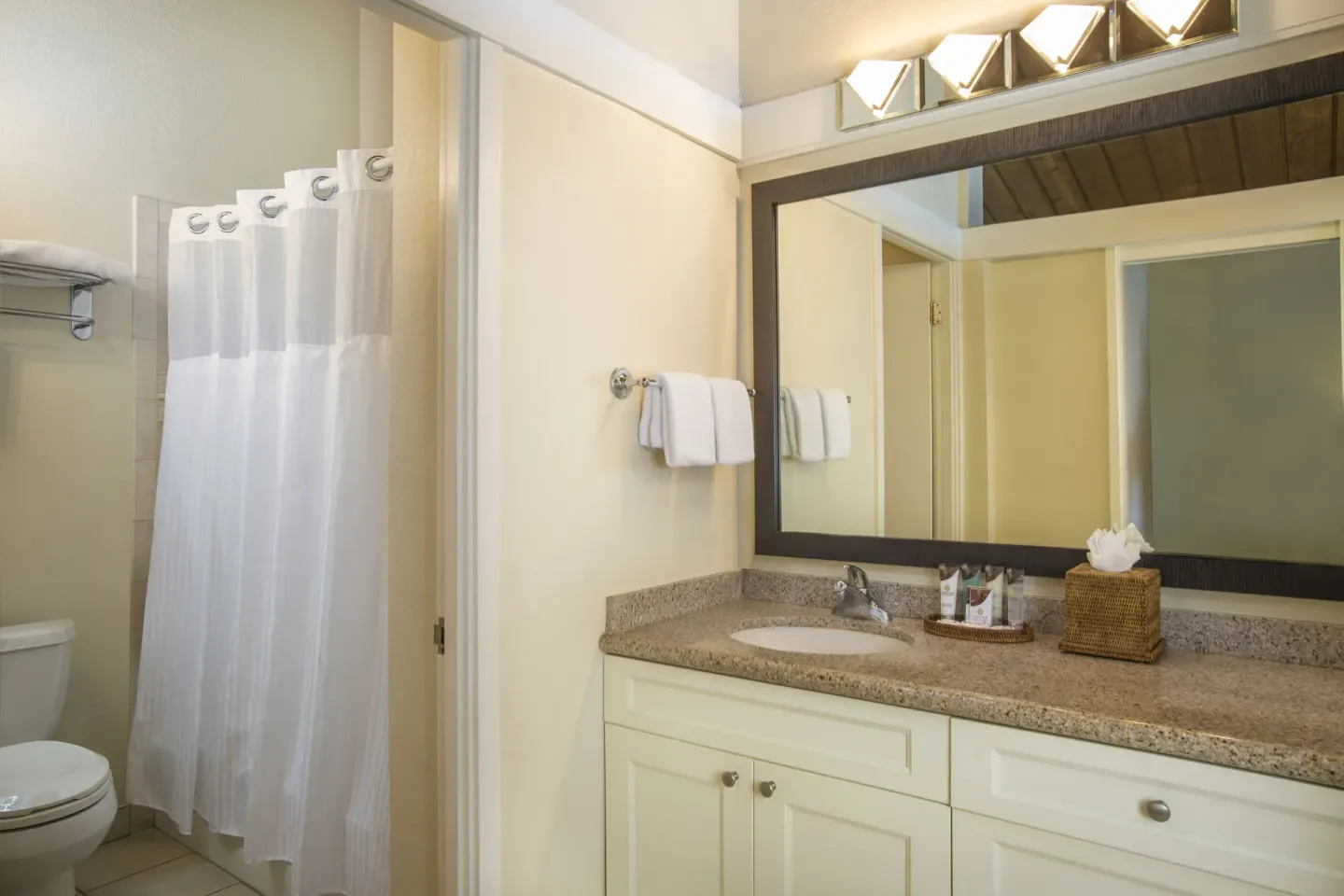 Deluxe Room bathroom with vanity, mirror, shower curtain, and towels at Napili Kai Beach Resort.
