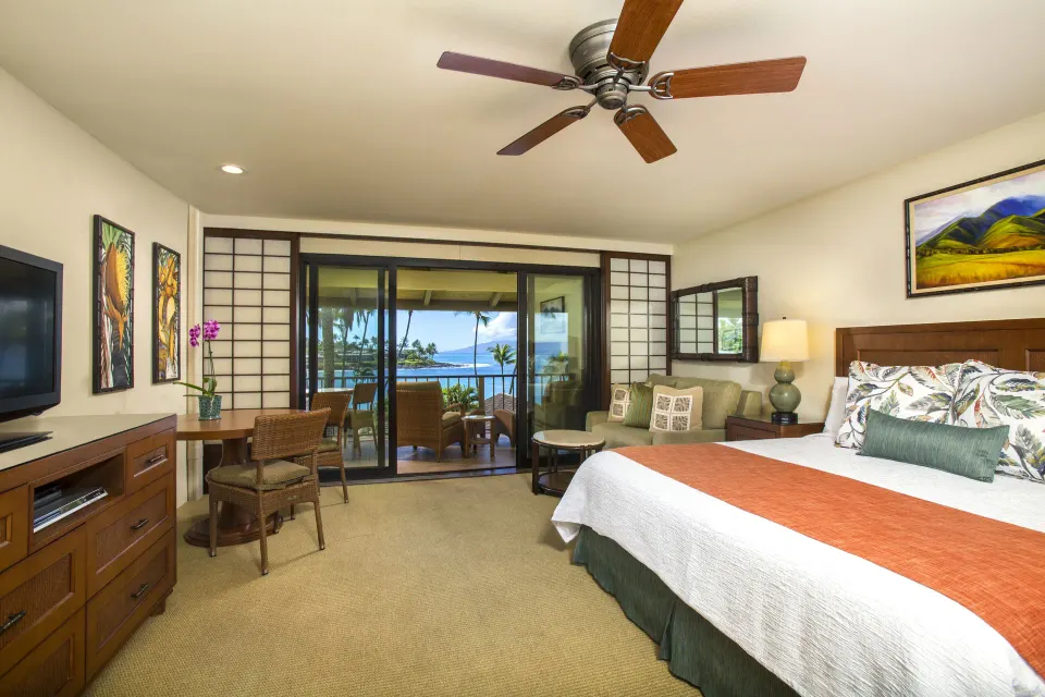 Deluxe Room with king bed, sofa, TV, and ocean-facing balcony at Napili Kai Beach Resort.