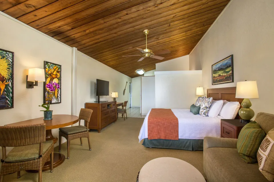 Deluxe Room with king bed, sofa, dining table, and vaulted wood ceiling at Napili Kai Beach Resort.